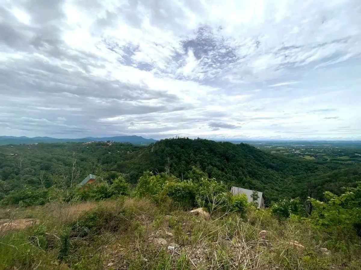 A sweeping view of rolling hills and distant mountains beneath a cloudy sky, evoking the majestic beauty of the Great Smoky Mountains. The landscape offers a sense of serenity and the promise of outdoor adventure.
