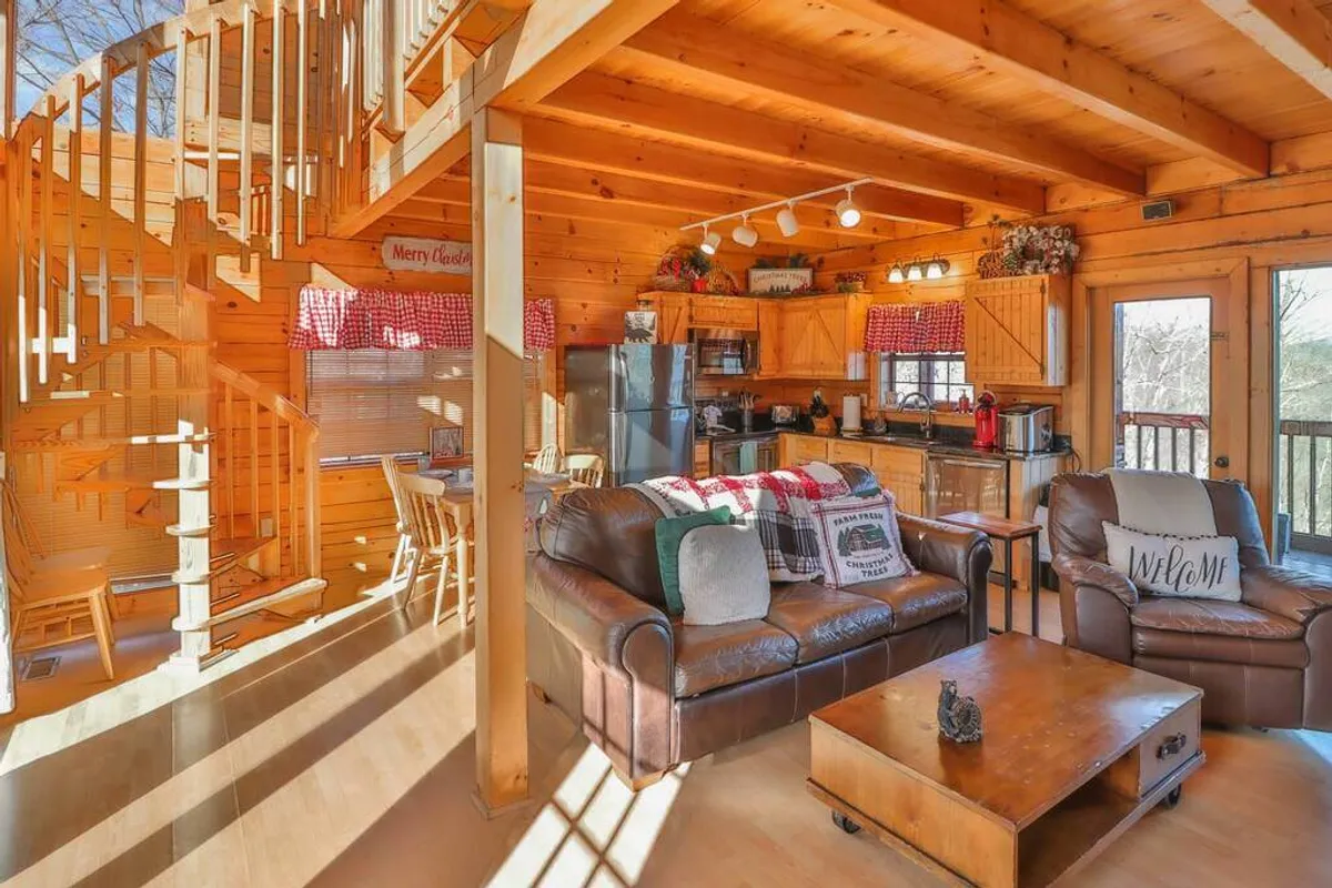 An inviting open-plan interior with a spiral staircase, leather sofa, visible kitchen area, and dining table. The space is styled for socializing and relaxation, evoking cozy evenings and shared family moments.