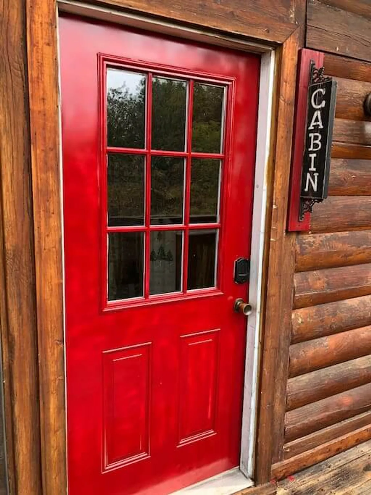 A charming cabin exterior with a red front door, wooden log construction, and a welcoming porch set amidst nature. The view offers a first impression of the cabin’s cozy and inviting setting, perfect for families setting off on nearby adventures.
