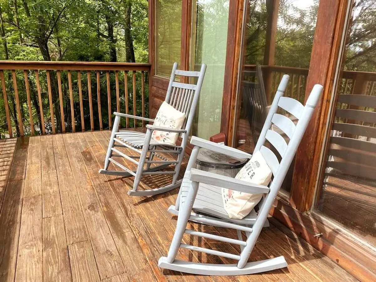 A wooden deck with comfortable rocking chairs, set against a backdrop of lush greenery. The setting sun bathes the area in warm light, inviting couples to relax, read, or simply take in the tranquil surroundings together.