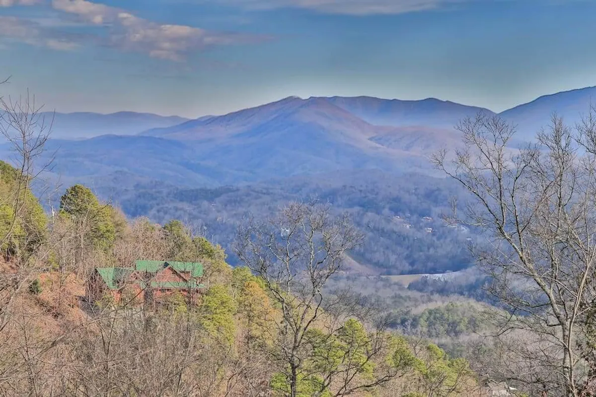 A scenic view from the cabin, showing a mountain range and a lush, wooded valley with the cabin's green roof visible. The tranquil setting perfectly captures the opportunity to watch sunsets, encounter wildlife, and enjoy stargazing—activities that foster lasting memories for all generations.
