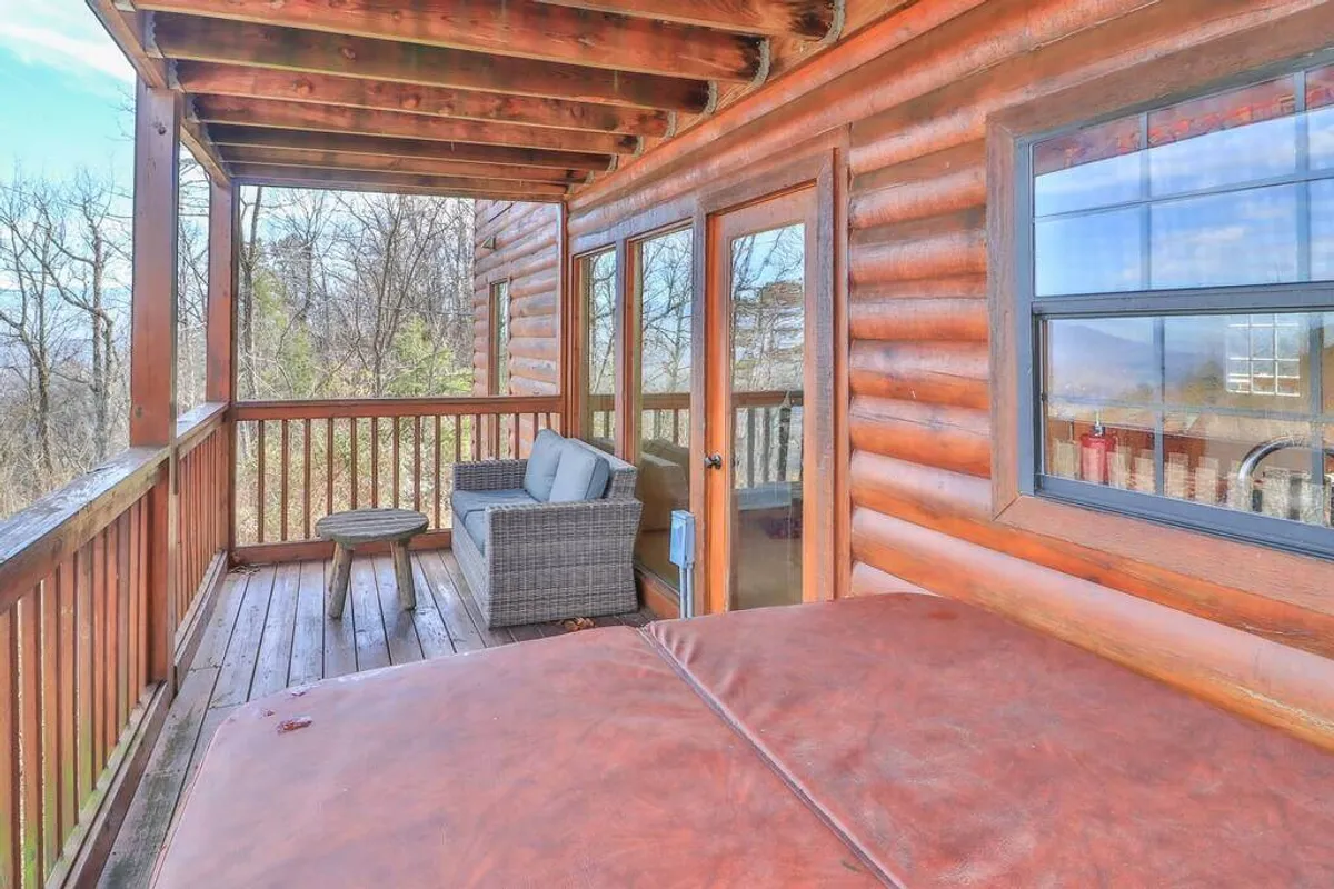This image showcases a spacious wooden deck surrounded by nature. A bubbling hot tub is the centerpiece, flanked by comfortable outdoor seating and a scenic view of the mountains. The area invites relaxation, with opportunities for socializing, sipping drinks, and soaking under the stars.