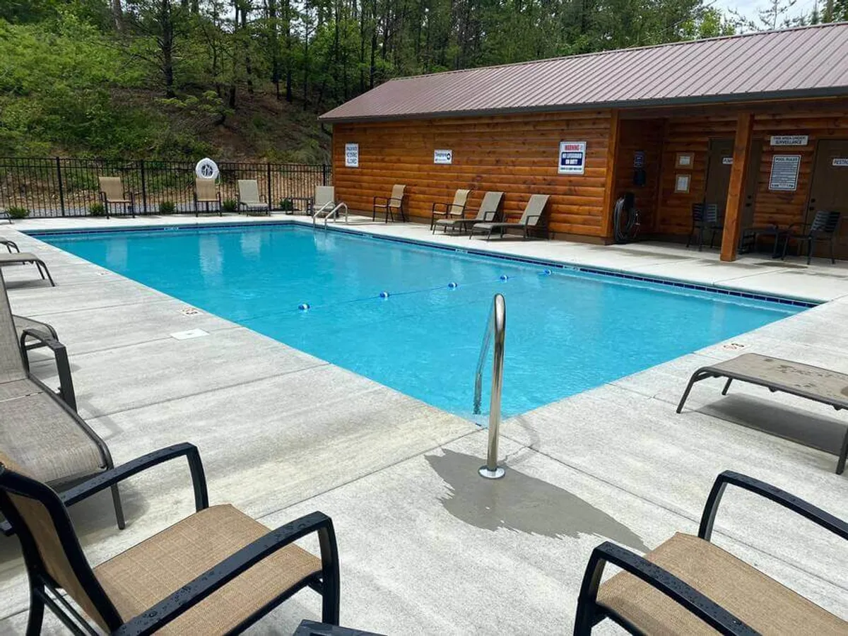 A community swimming pool surrounded by lounge chairs, with a wooden cabin and a fenced area nearby. The pool area appears inviting and well-maintained, offering guests a spot to refresh, socialize, or simply relax after a day of exploration.